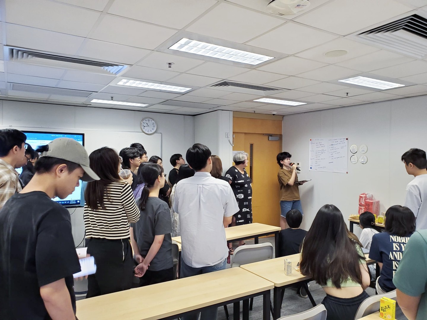 Clare Narrod standing with Hong Kong Polytechnic students, observing a presentation.