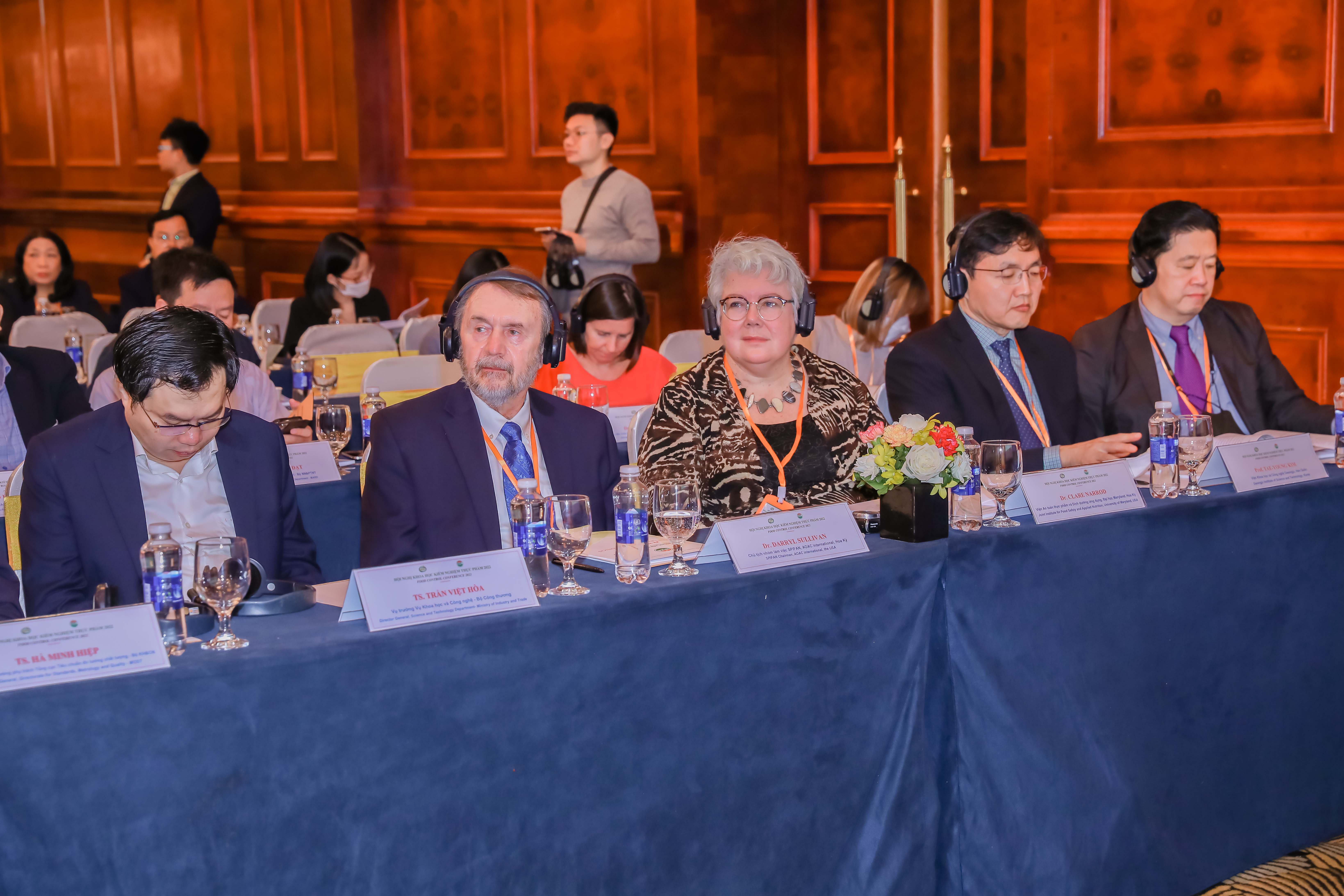 Dr. Clare Narrod and conference participants seated at a table wearing headphones and listening to a presentation.